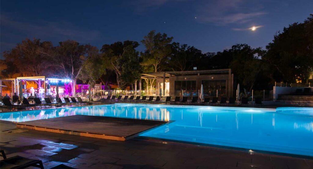 Piscine illuminée et bar à la tombée de la nuit, camping 5 étoiles en Corse